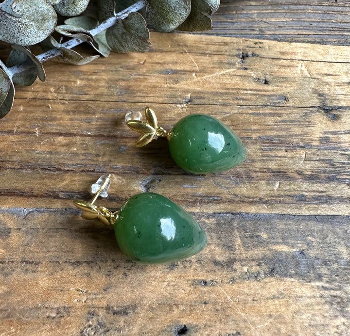 Green jade teardrop earrings with gold leaf caps resting on a weathered wooden surface.