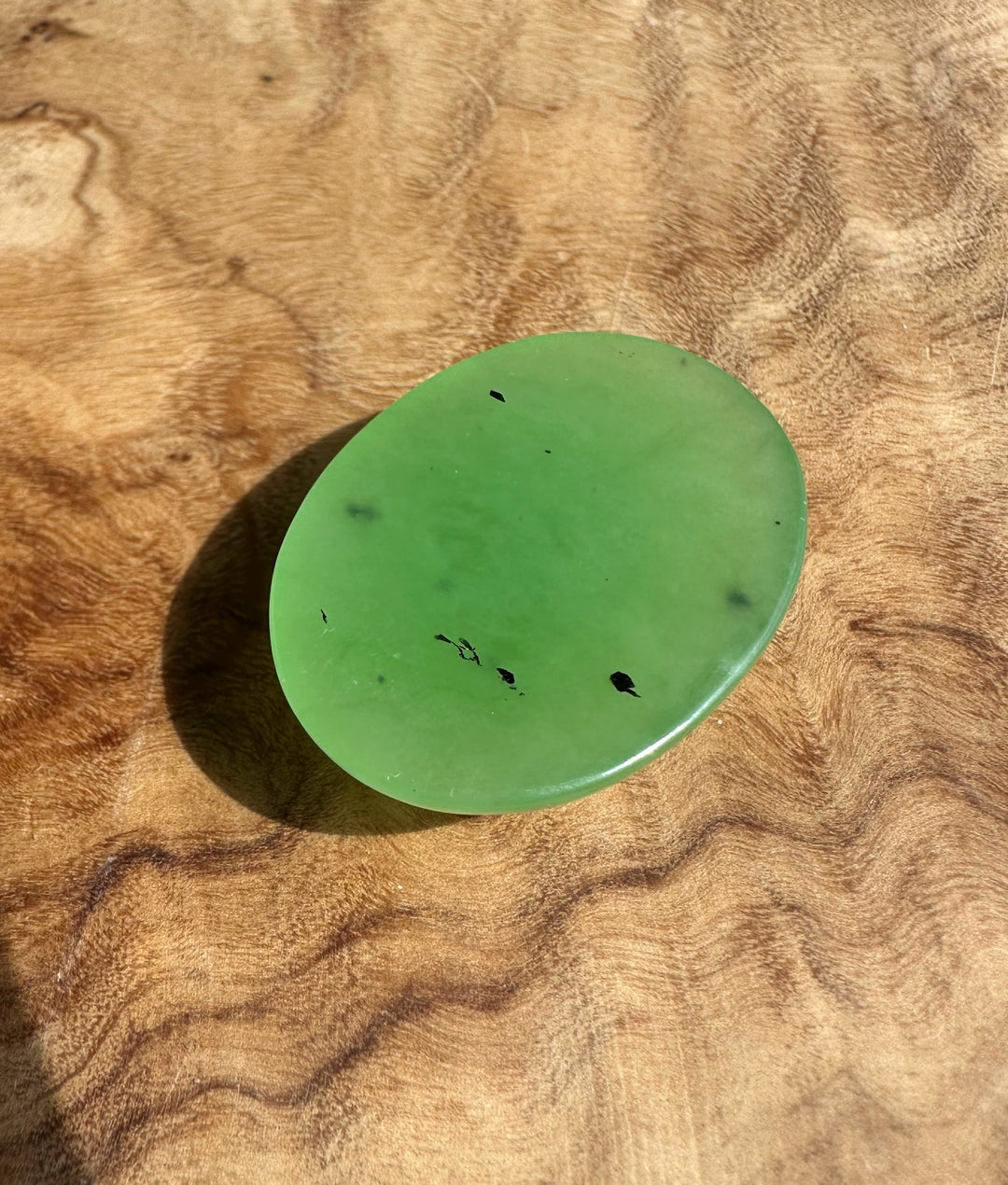 Oval apple green cabochon gemstone measuring 30x22mm on a wooden surface.