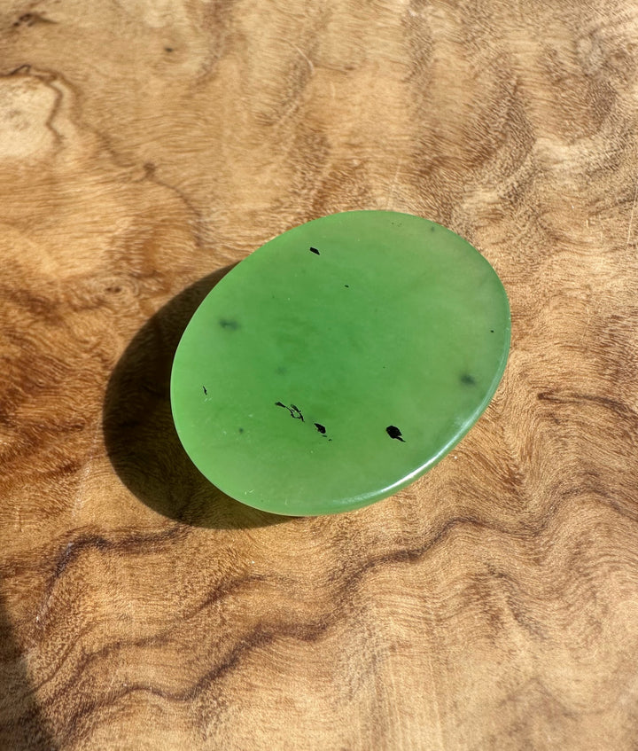 Oval apple green cabochon gemstone measuring 30x22mm on a wooden surface.