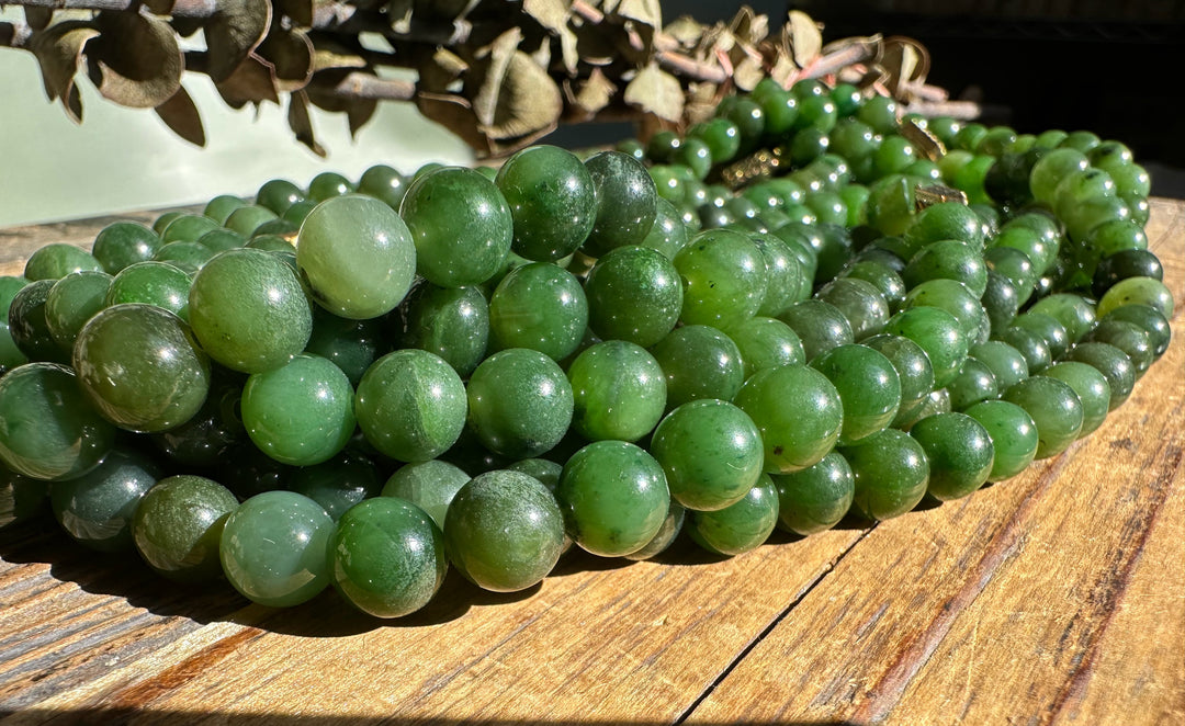 Multiple strands of green nephrite jade beads stacked on a weathered wooden surface with dried leaves overhead