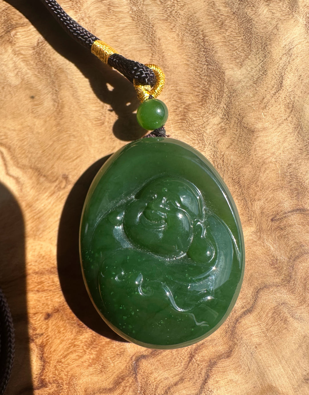 Green jade pendant with Buddha carving on a wooden surface