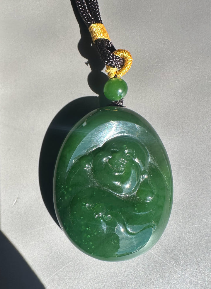 Green jade pendant with Buddha carving on a black cord against a gray background
