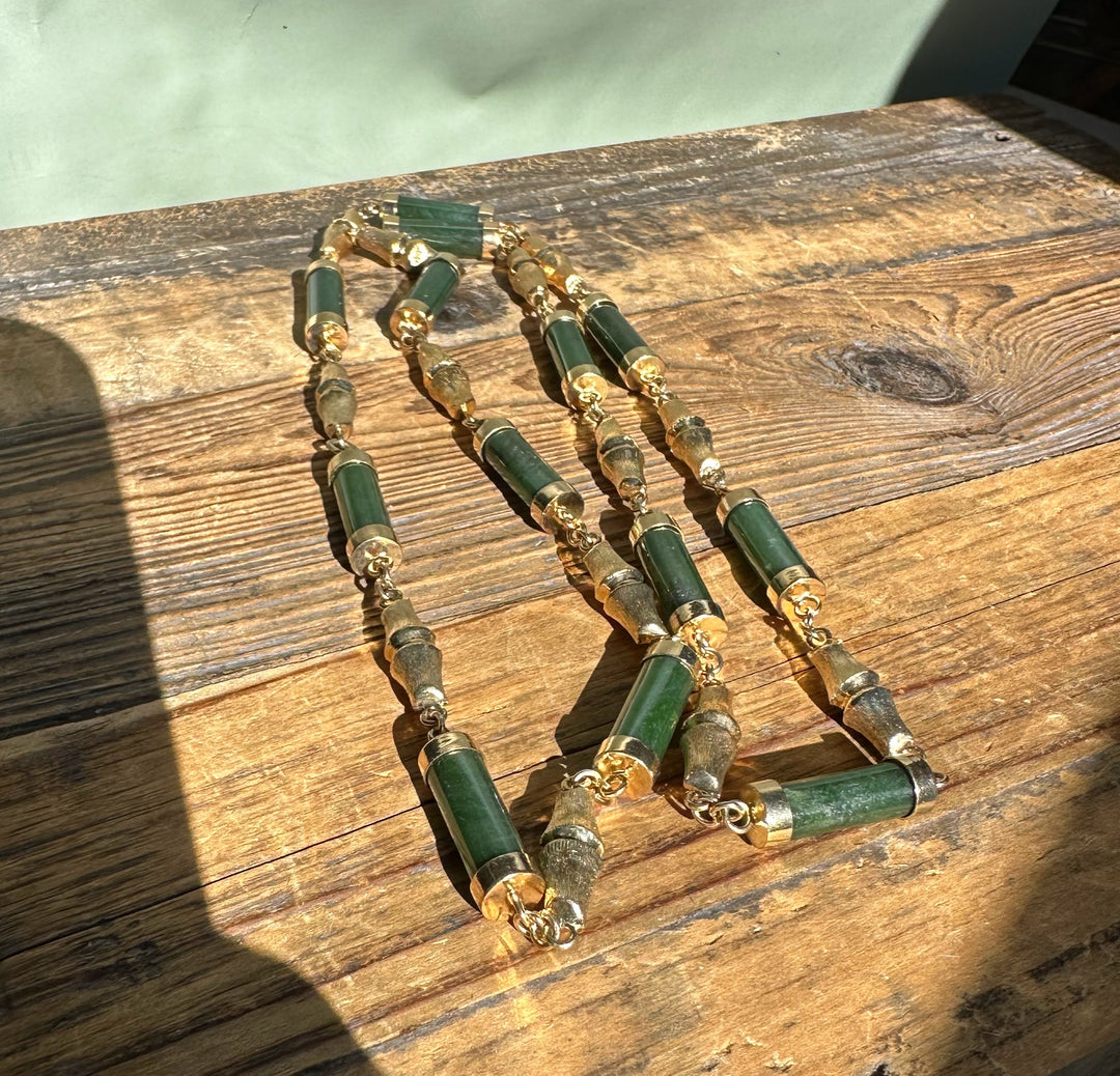 Green jade bead necklace with gold spacers and chain sections displayed on a sunlit rustic wood surface