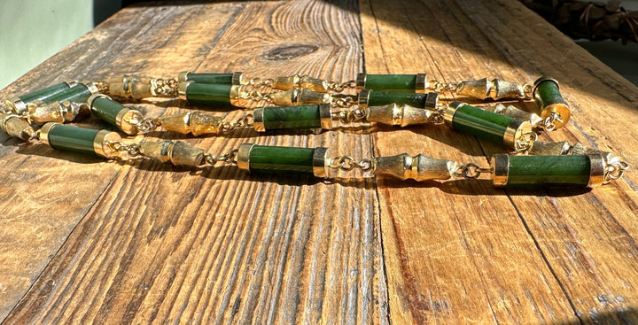 Vintage jade necklace with green cylindrical beads and gold caps laid on a weathered wooden table