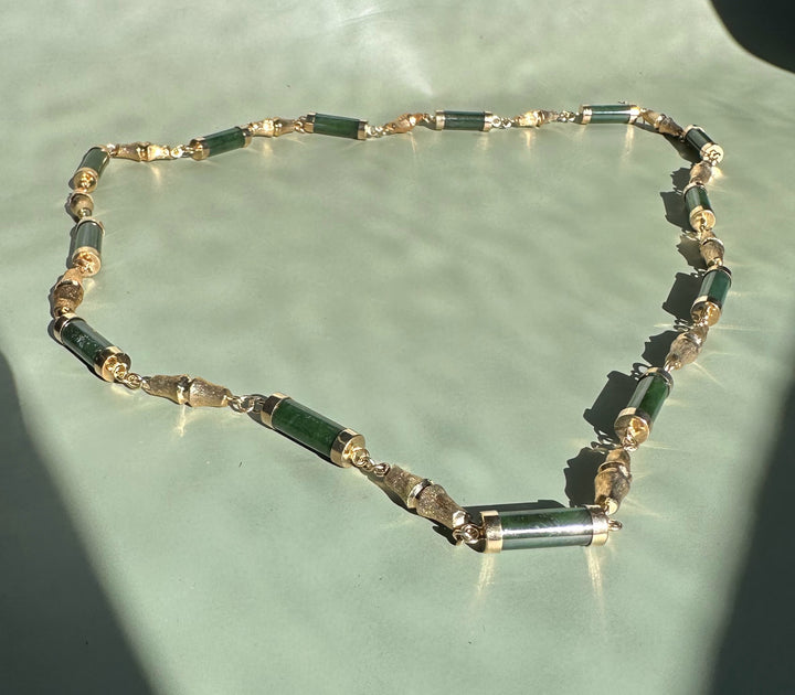 Close up of vintage jade necklace showing green tube beads with gold caps connected by delicate metal links on a pale green backdrop