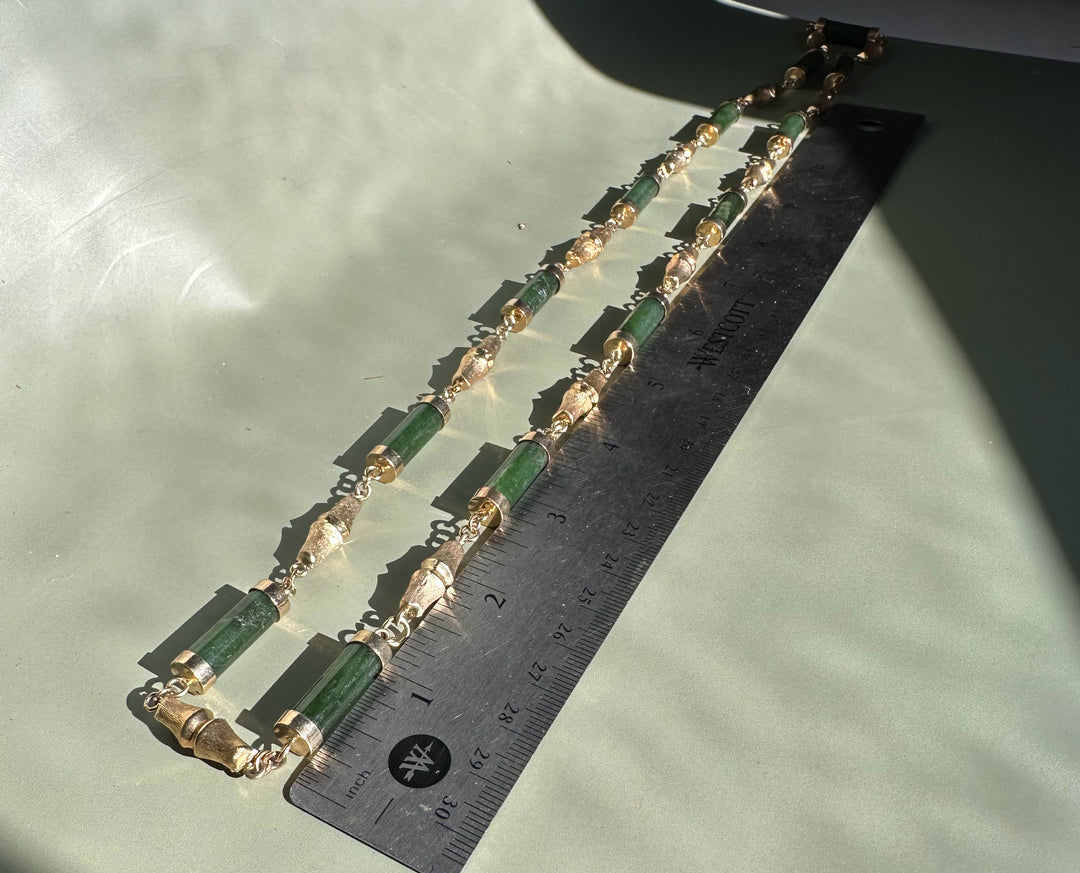 Double strand vintage jade necklace featuring green cylindrical beads and ornate gold spacers on a pale green background with a ruler
