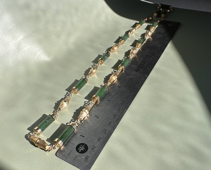 Double strand vintage jade necklace featuring green cylindrical beads and ornate gold spacers on a pale green background with a ruler