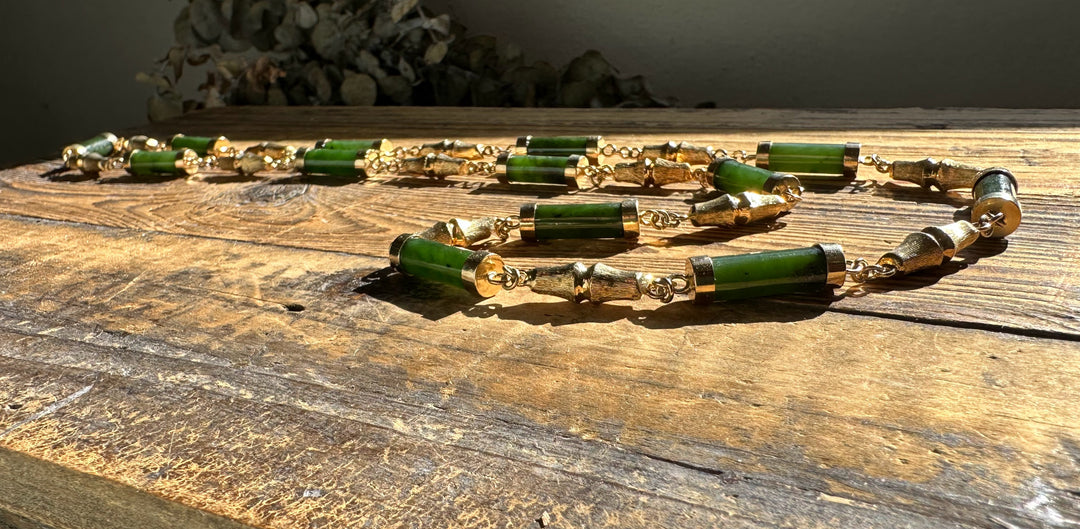Vintage Jade Necklace with green cylindrical beads and gold spacers laid across a rustic wooden surface