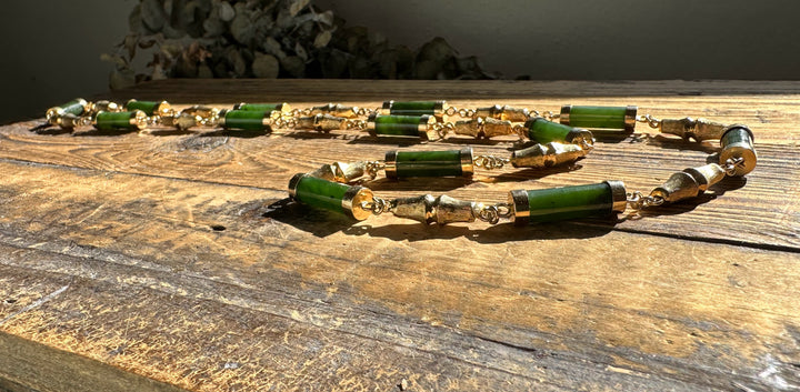 Vintage Jade Necklace with green cylindrical beads and gold spacers laid across a rustic wooden surface
