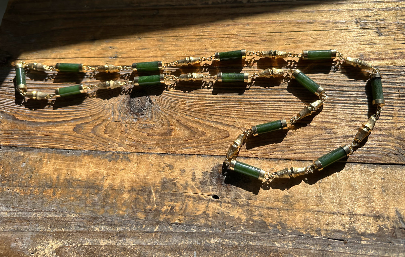 Vintage Jade Necklace with green beads and gold accents arranged in a loose loop on a wooden surface