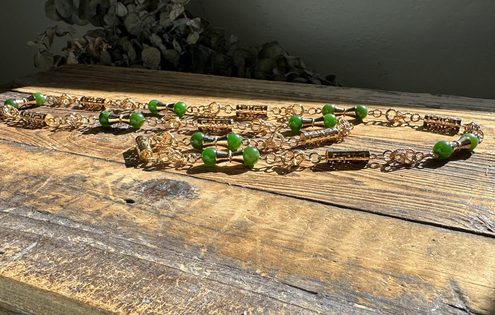 Top view of green jade necklace with gold metal ends on a weathered wooden table with dried foliage nearby