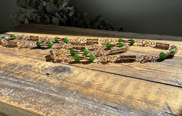 Top view of green jade necklace with gold metal ends on a weathered wooden table with dried foliage nearby