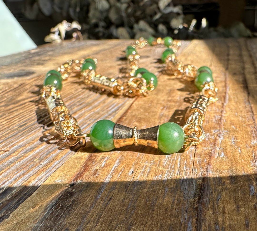 Vintage jade bead necklace with green stones and gold ornate links on a rustic wooden surface