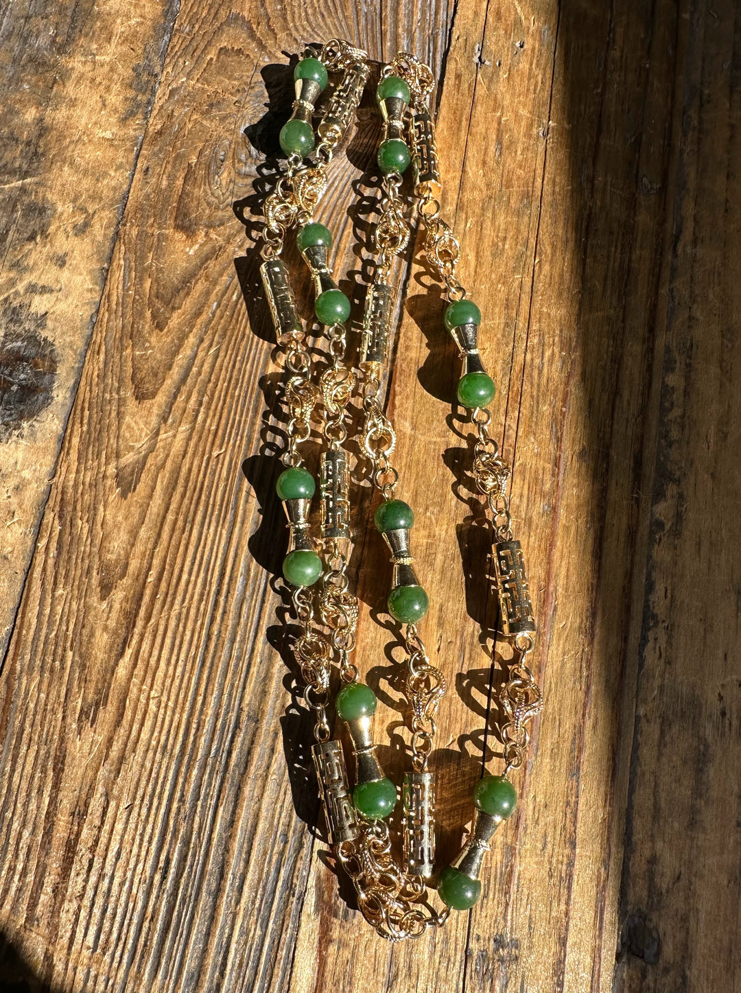 Tangled gold chain necklace with green jade beads resting on a wooden surface.