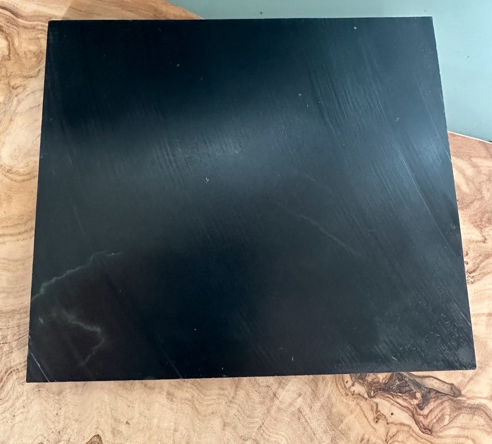 Wyoming Jade Slab resting on a wooden surface, a square black stone.