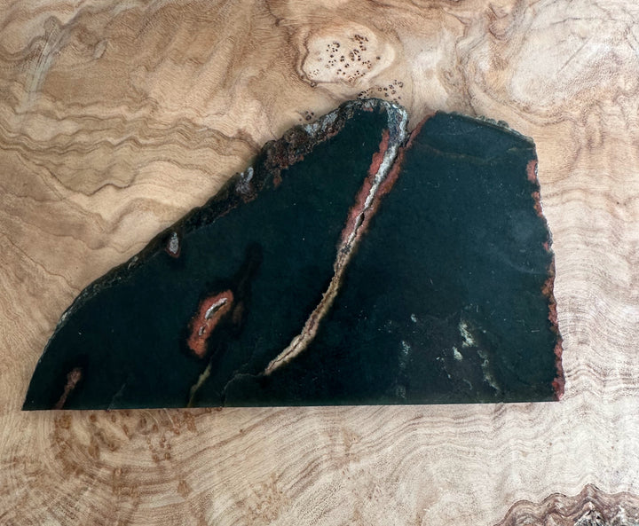 Wyoming Jade Slab 105g dark green piece with a rusted fracture along the edge on wood.