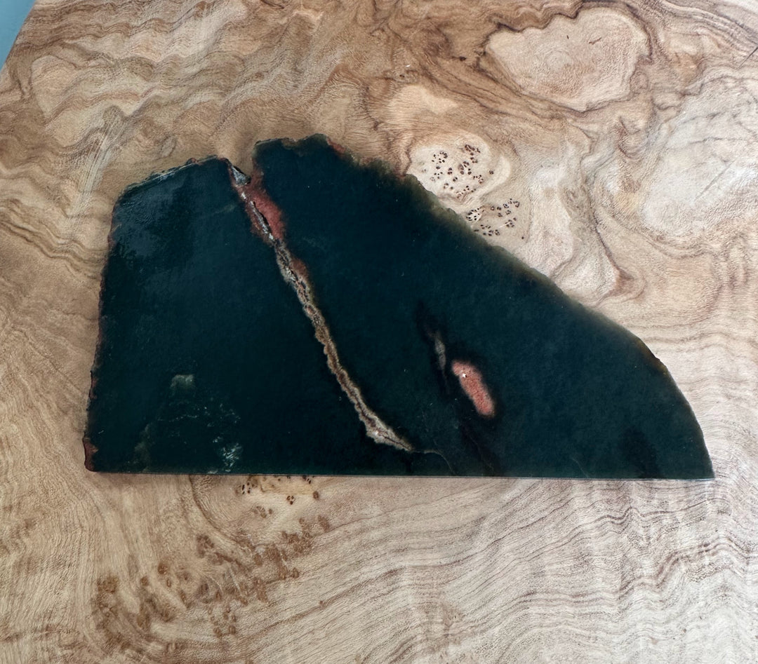 Wyoming Jade Slab 105g dark green with a diagonal rust vein and reddish patches on a wood surface.
