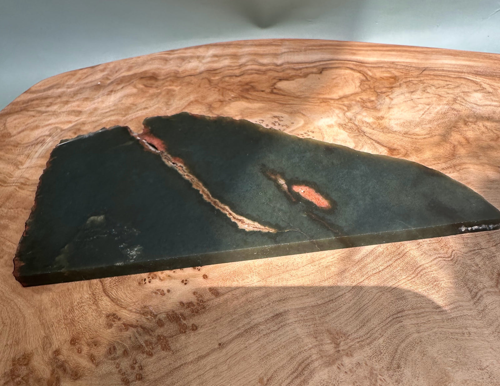 Dark Wyoming Jade slab with a diagonal coppery seam and exposed rough edge on a wood surface