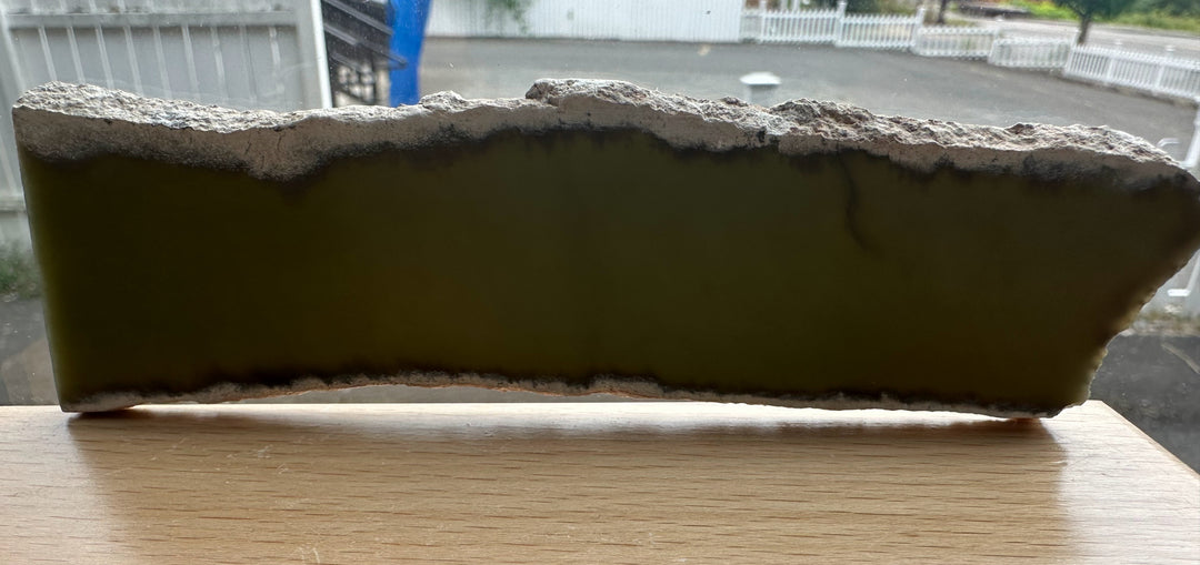 Wyoming Slab 50g rough edged slab with green interior set on a wooden table by a window.