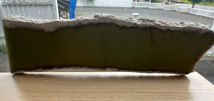 Wyoming Slab 50g rough edged slab with green interior set on a wooden table by a window.