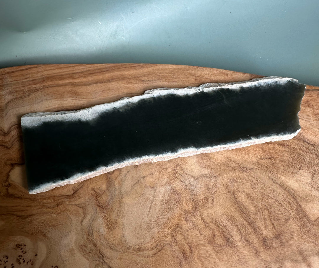 Wyoming Slab 50g elongated dark slab with a white ragged edge on a wooden surface.