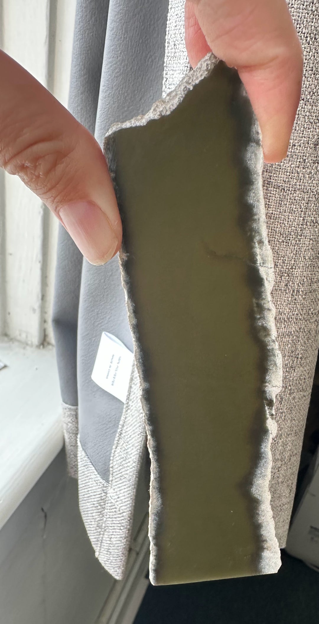 Close up of Wyoming Slab 50g being pinched between fingers, showing a greenish gray interior and a jagged edge