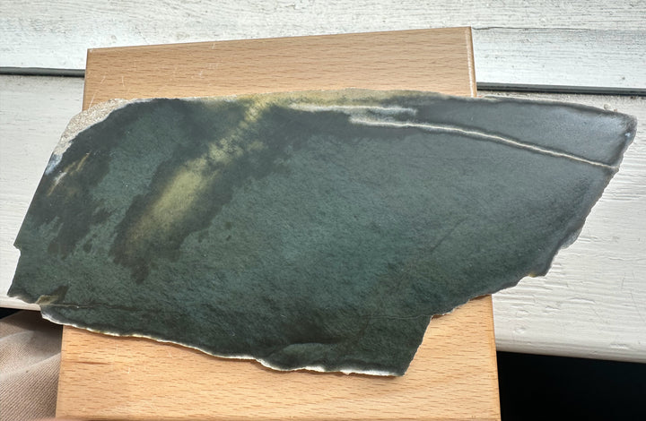 Wyoming Slab 230g laid on a wooden surface, dark slate with a greenish tint and rough light edge