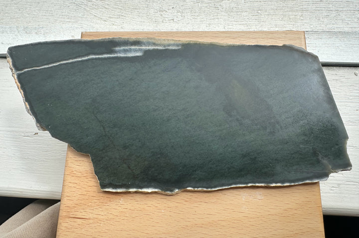 Top view of Wyoming Slab 230g with deep green slate and a pale edge along the bottom resting on wood