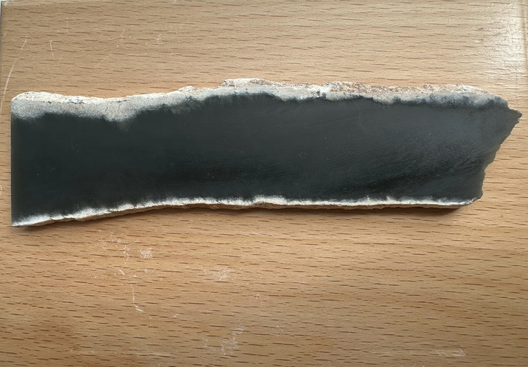 Wyoming Slab 50g with a dark charcoal center and a rough light gray edge on a wooden table.