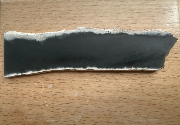 Wyoming Slab 50g with a dark charcoal center and a rough light gray edge on a wooden table.