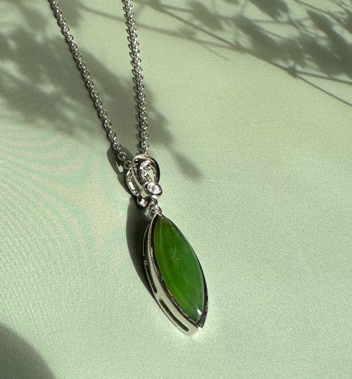 Green jade pendant with CZ set in a silver bezel on a silver chain against pale green fabric