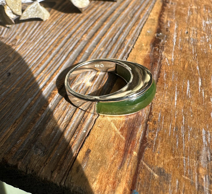 Silver ring with a green jade inlay rests on a weathered wooden surface