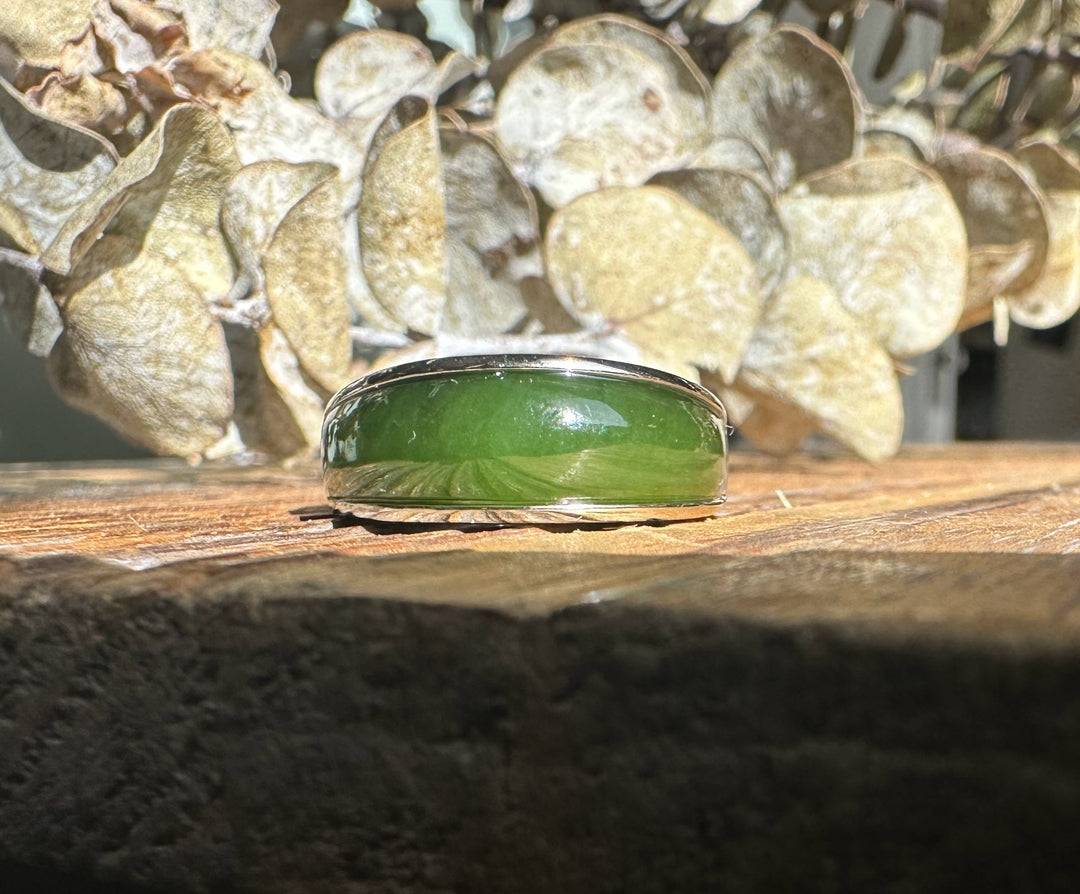 Canadian Jade Ring with a glossy green jade cabochon in a silver setting on a rustic wooden surface