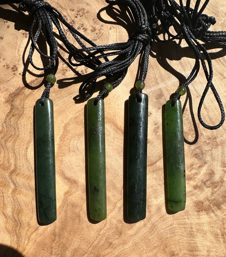 Four rectangular jade pendants on black cords with small green beads against a wood background