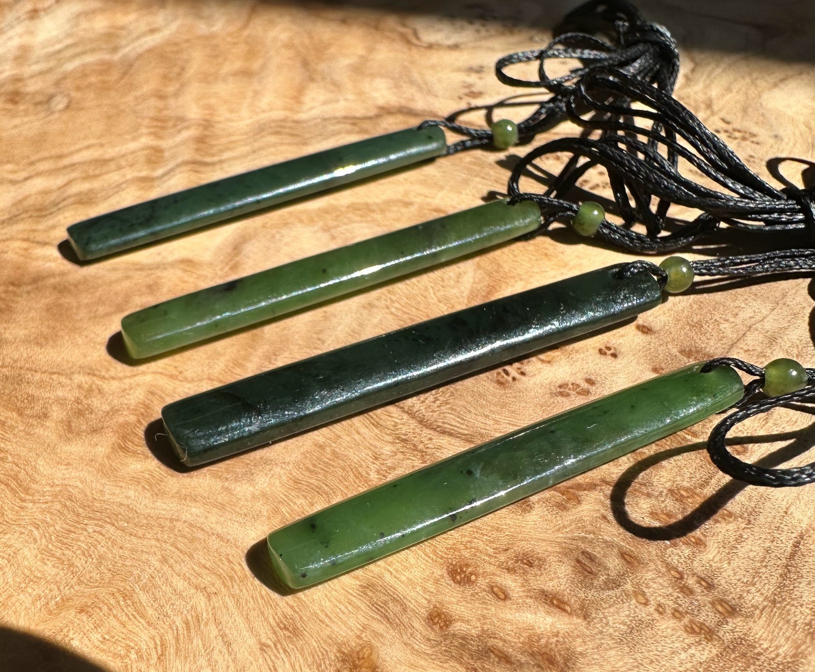 Four green jade drop pendants with black cords laid on a wooden surface