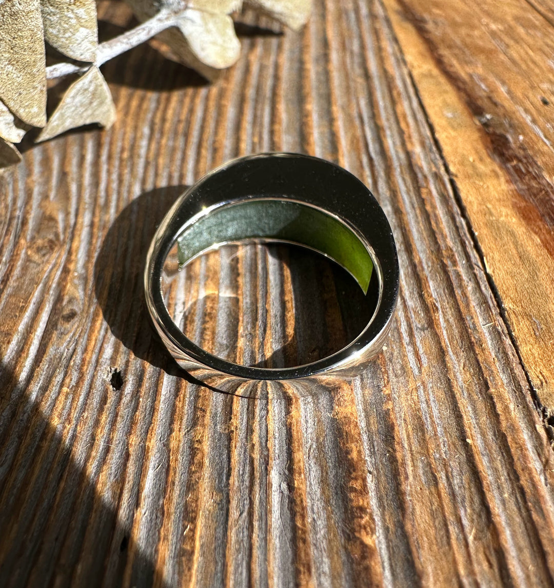 Canadian Jade Ring 3399 silver band with a green jade inlay resting on a rustic wooden surface
