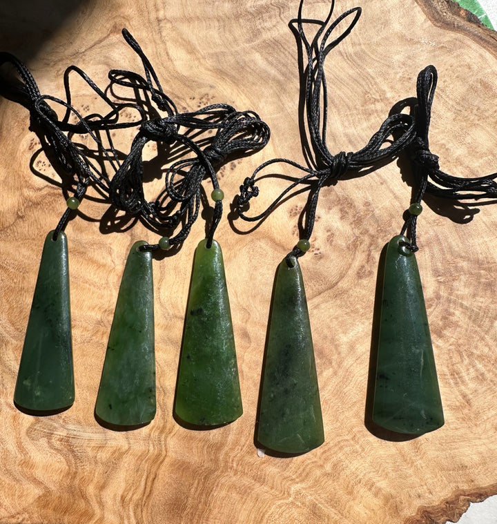 Row of green jade drop pendants on black cords with small beads, laid on a wooden surface.