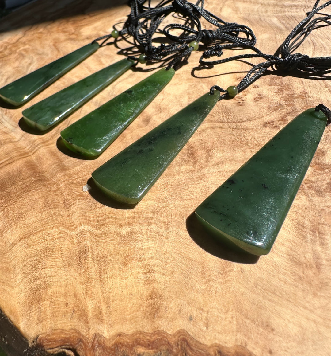 Row of five green jade drop pendants on black cords spread across a wooden surface
