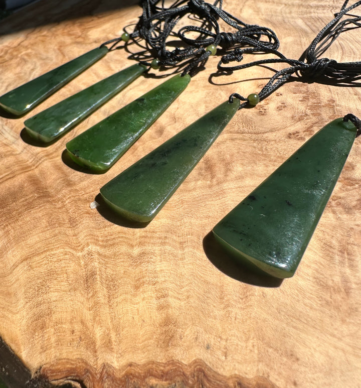 Row of five green jade drop pendants on black cords spread across a wooden surface