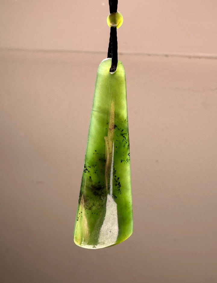 Long green jade drop pendant with a hole at the top, hanging on a black cord with a small yellow bead