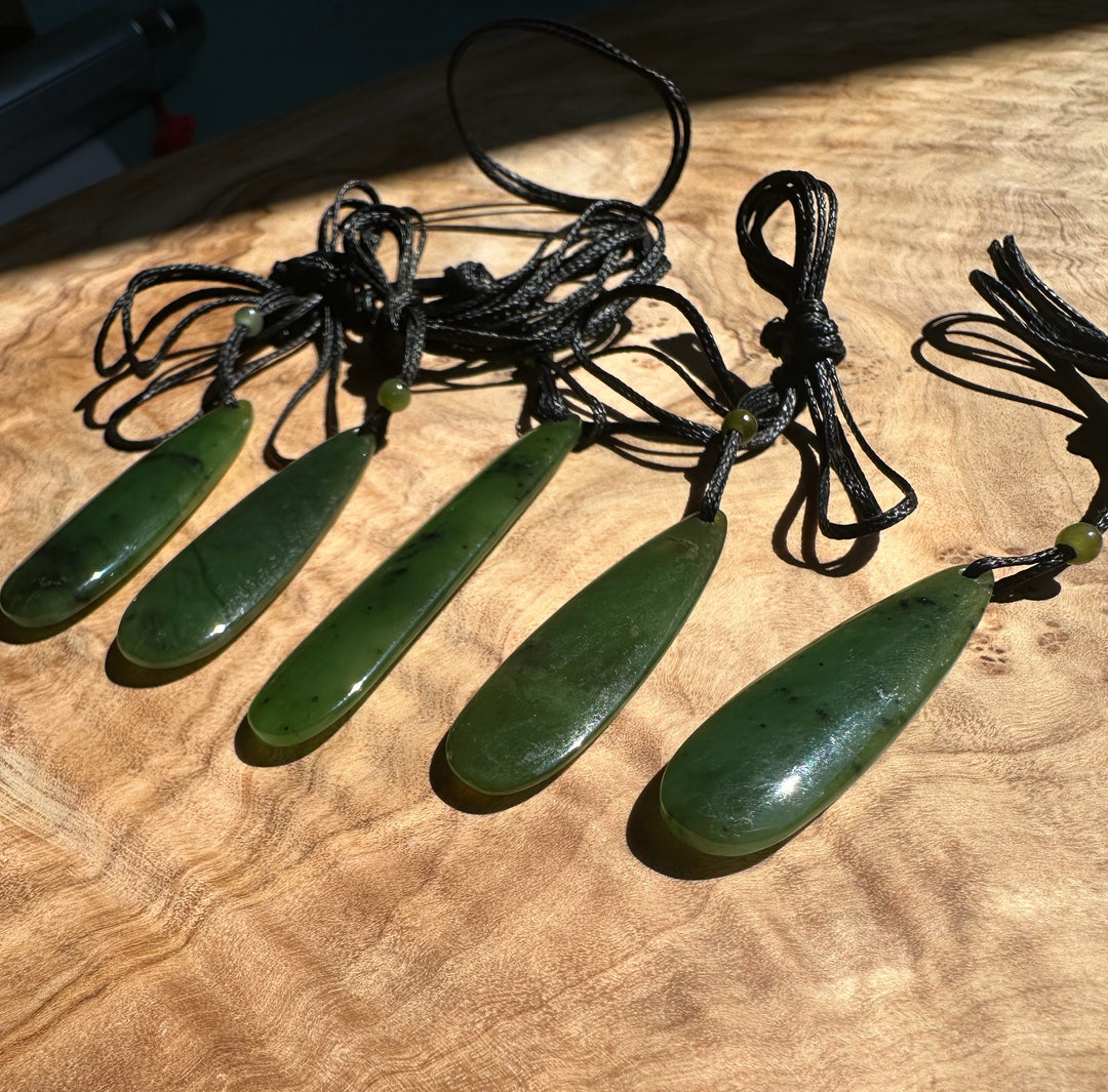 Five jade teardrop pendants on black cords laid out on a wooden surface