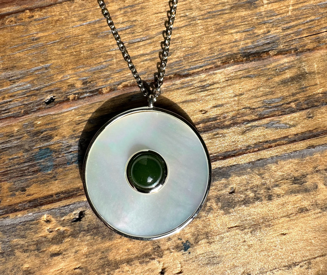 Circular pendant with a mother of pearl disk and a green jade center in a silver bezel on a chain