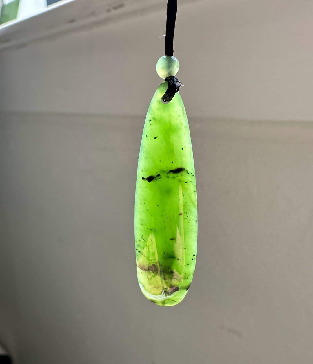 Long lime green jade pendant with a small round bead above on a black cord