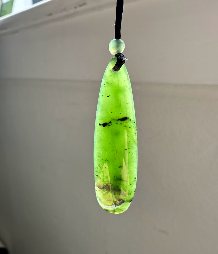 Long lime green jade pendant with a small round bead above on a black cord