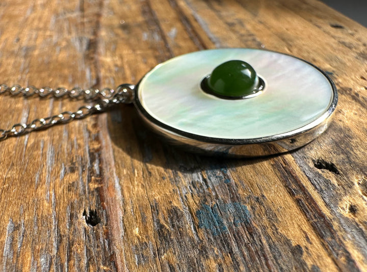 Side view of round mother of pearl pendant with green jade center resting on a rustic wooden table