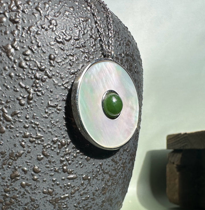 Close up of round mother of pearl pendant featuring a green jade centerpiece on a textured surface