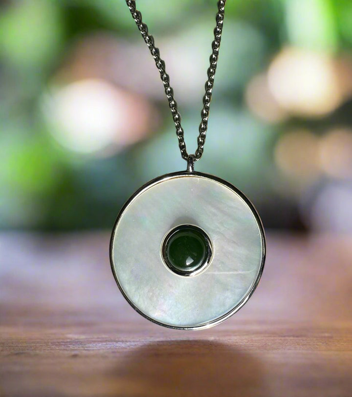 Circular mother of pearl pendant with a green jade center on a silver chain