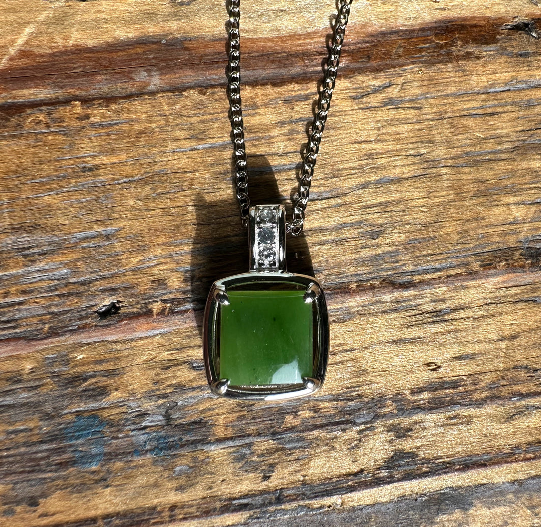 Close-up of green jade pendant on a wooden surface showing the square jade in a silver mount with CZ-studded bail