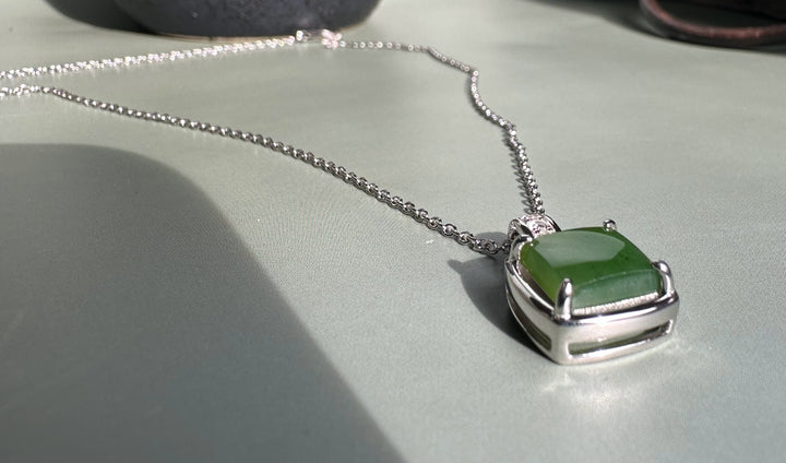 Canadian Jade Pendant with CZ on a silver chain with a diamond-studded bail resting on a pale backdrop.