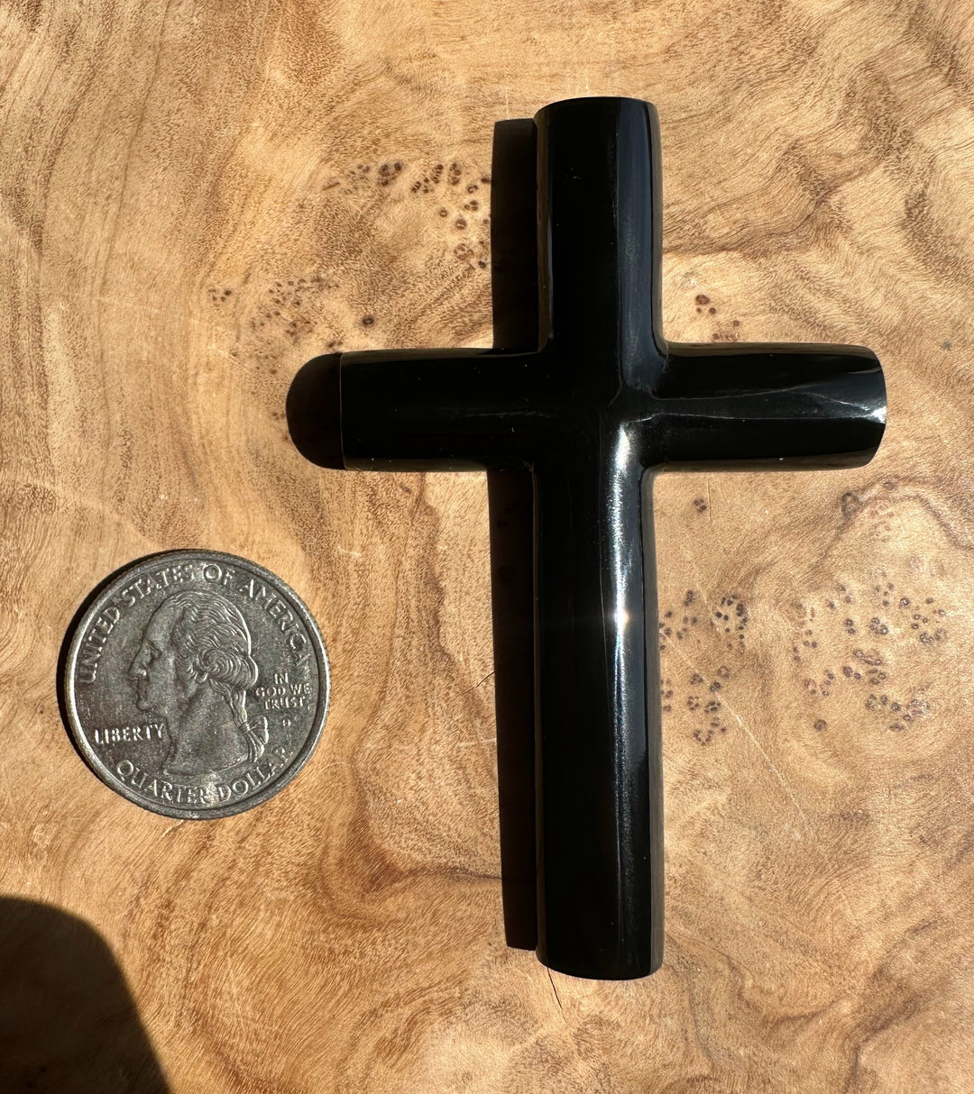 Black cross next to a quarter on a wooden surface